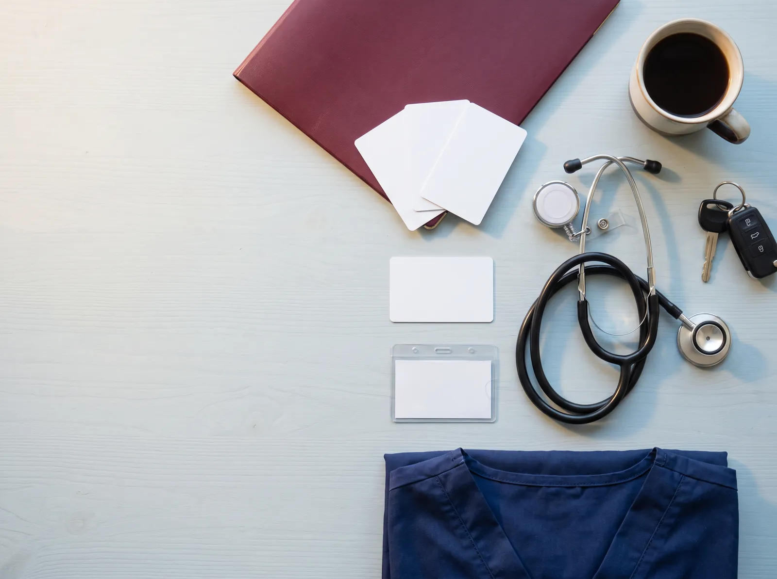 A nurse's badge, stethoscope, scrubs and keys laid out on a table